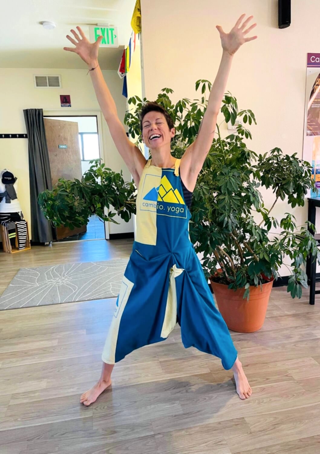Jenn with her eyes closed, a huge grin and her hands up in the air wearing a Cambio onsie. 